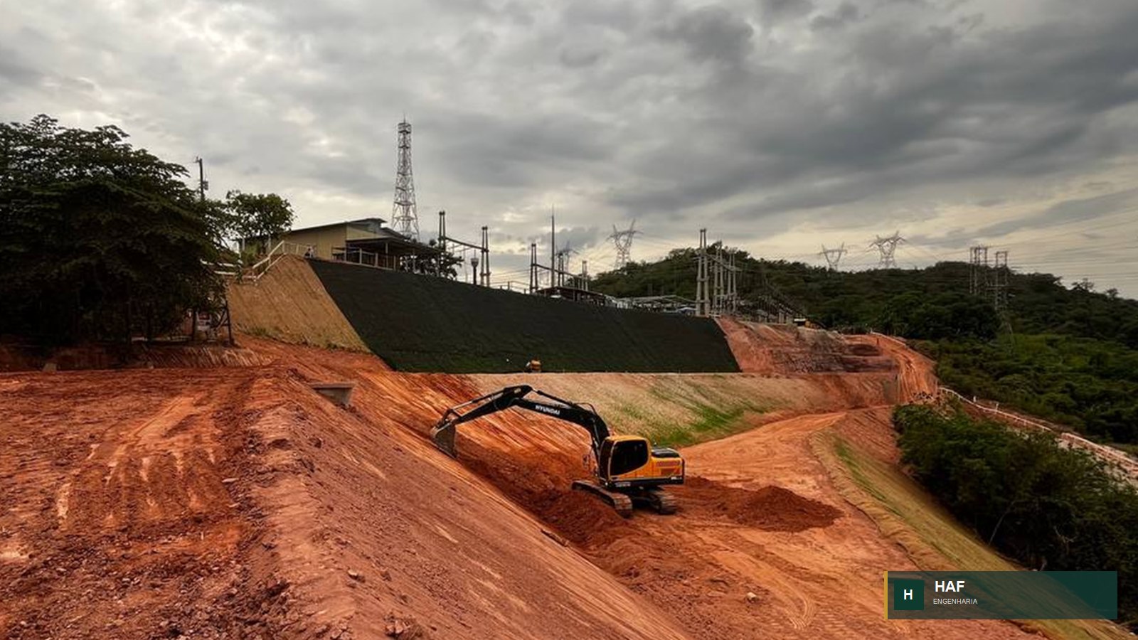 Escavadeira em serviço de terraplenagem com conformação de talude e plataforma de obra